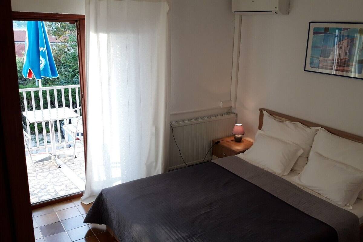 A bedroom with a bed, two bedside tables with lamps, a radiator, and a window with curtains.