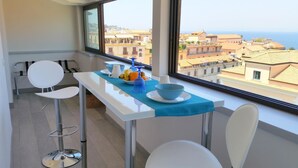 A modern kitchen with a view of the sea, a dining table with chairs, and a blue tablecloth. - B&B Unique (Sorrento)