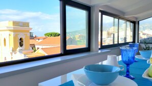 A room with large windows, a table with blue bowls, and a view of buildings and trees. - B&B Unique (Sorrento)