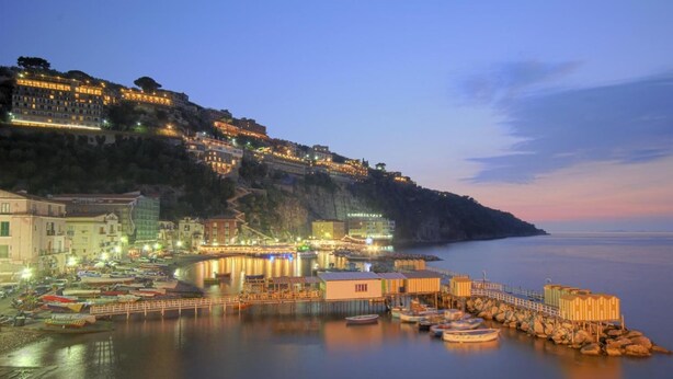 A coastal town at dusk with buildings along the waterfront, a pier, and boats docked. - B&B Unique (Sorrento)