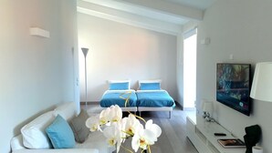 A modern bedroom with a bed, a white sofa, a TV, and a vase of white flowers. - B&B Unique (Sorrento)