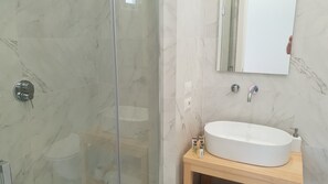 A bathroom with a glass shower enclosure, a white sink, and a mirror above it. - Younique (Sorrento)