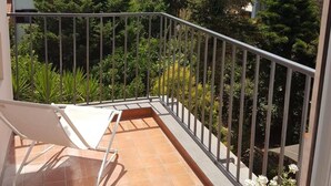 A balcony with a white chair, a tiled floor, and a view of a hillside with buildings and trees. - Younique (Sorrento)