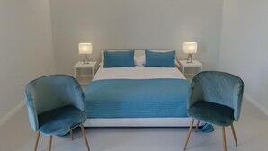 A modern bedroom with a large bed, two bedside tables with lamps, and two matching armchairs. - Younique (Sorrento)