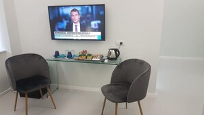 A modern office space with a glass desk, two grey chairs, a television displaying a news channel, and a coffee maker. - Younique (Sorrento)