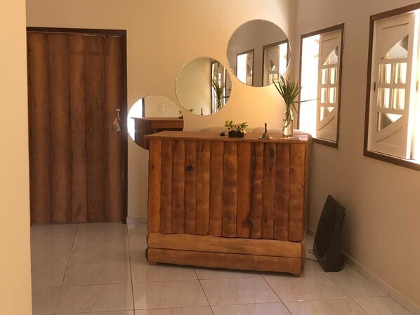 A wooden cabinet with mirrors and a vase of flowers in a hallway with tiled flooring and a closed wooden door. - Pousada São Miguel dos Milagres (São Miguel dos Milagres)