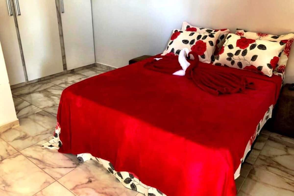 Ein Schlafzimmer mit rotem Bettbezug, floralen Kissen und einer weißen Decke.