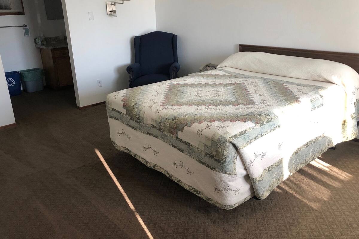 A bedroom with a bed, a chair, and a small desk.