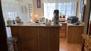 Cozinha com armários de madeira, cafeteira, computador e janela com cortinas leves.