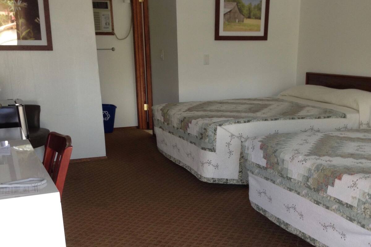 A room with two beds, a desk, and a chair. There is a door leading to another room.