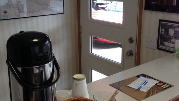 Máquina de café, cesta com xícaras, um copo e um cardápio em uma bancada.