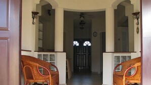 A hallway with two wicker chairs, a ceiling fan, and a door leading to another room. - Maya's Bajan Villas - Unit A (Oistins)