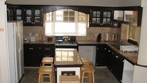A kitchen with dark cabinets, a central island with stools, a stove, and a window. - Maya's Bajan Villas - Unit A (Oistins)