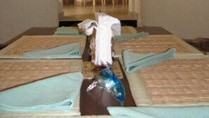 A hotel room with a large bed, a small table, and a view of the kitchen and dining area. - Maya's Bajan Villas - Unit A (Oistins)