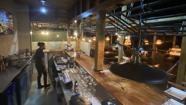Una zona de bar con una barra larga, taburetes y diversos utensilios.