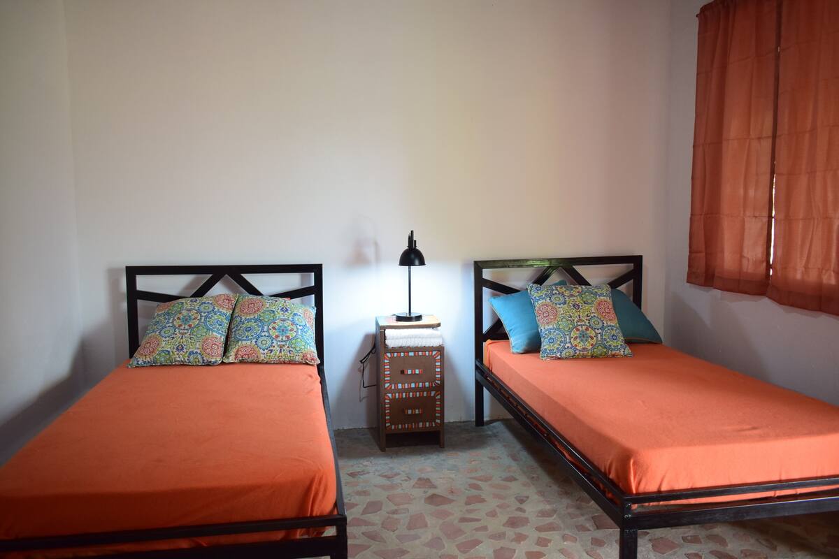 Una habitación pequeña con dos camas individuales, cada una con almohada estampada y ropa de cama naranja.