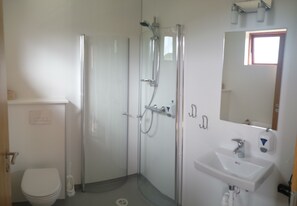 A bathroom with a toilet, a shower enclosure, and a sink with a mirror. - Guesthouse Hvitafell (Laugar)