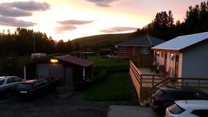 A parking area with a small building, a covered deck, and a grassy field. - Guesthouse Hvitafell (Laugar)