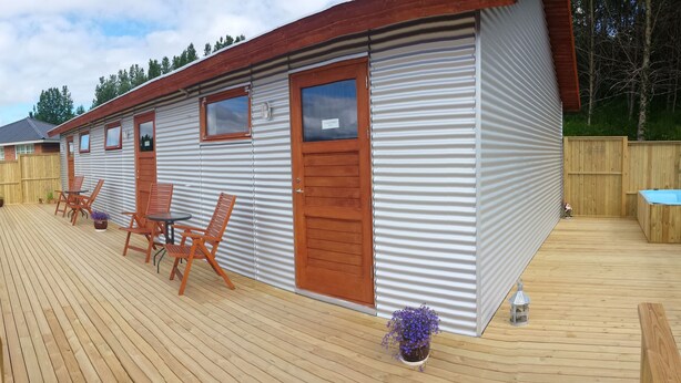 A mobile home with a deck, wooden furniture, and a small garden area. - Guesthouse Hvitafell (Laugar)