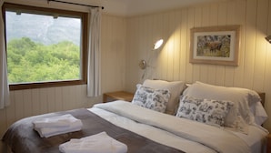 Una cama bien hecha con ropa blanca y una manta marrón, una mesita de noche con una lámpara y un cuadro en la pared.