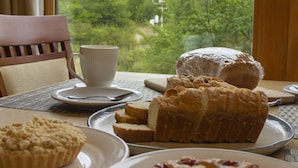 Una mesa con pasteles y una taza, una silla y vistas de montañas a través de una ventana.
