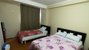 Habitació d'hotel amb dos llits, un més gran i un més petit, amb roba de llit floral. Té un terra de fusta i una cortina a la finestra.