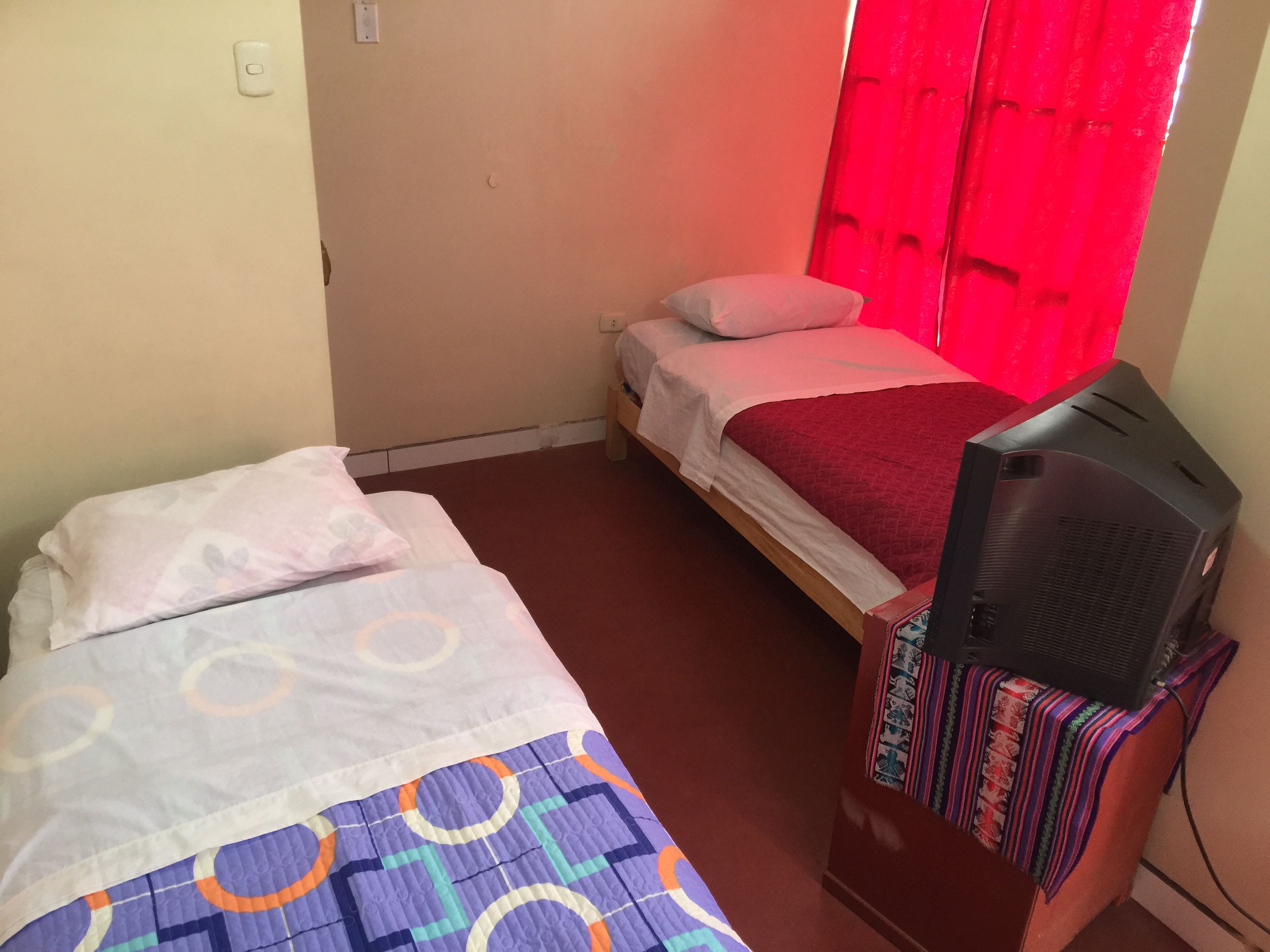 Ein kleines Zimmer mit zwei Betten, einem Fernseher auf einem Tisch und einem roten Vorhang.