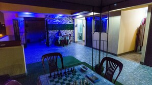 Una habitació amb un tauler d'escacs damunt d'una taula, una taula petita amb una planta i una cadira.