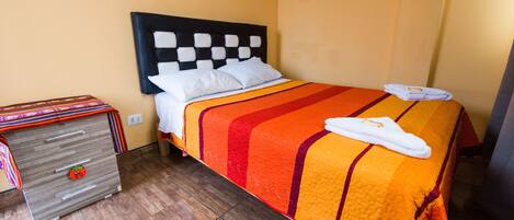 A hotel room with a bed, a wooden dresser, and a wall socket.