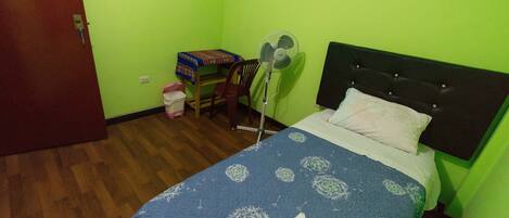 Una habitación con cama, una silla, una mesa y un ventilador.