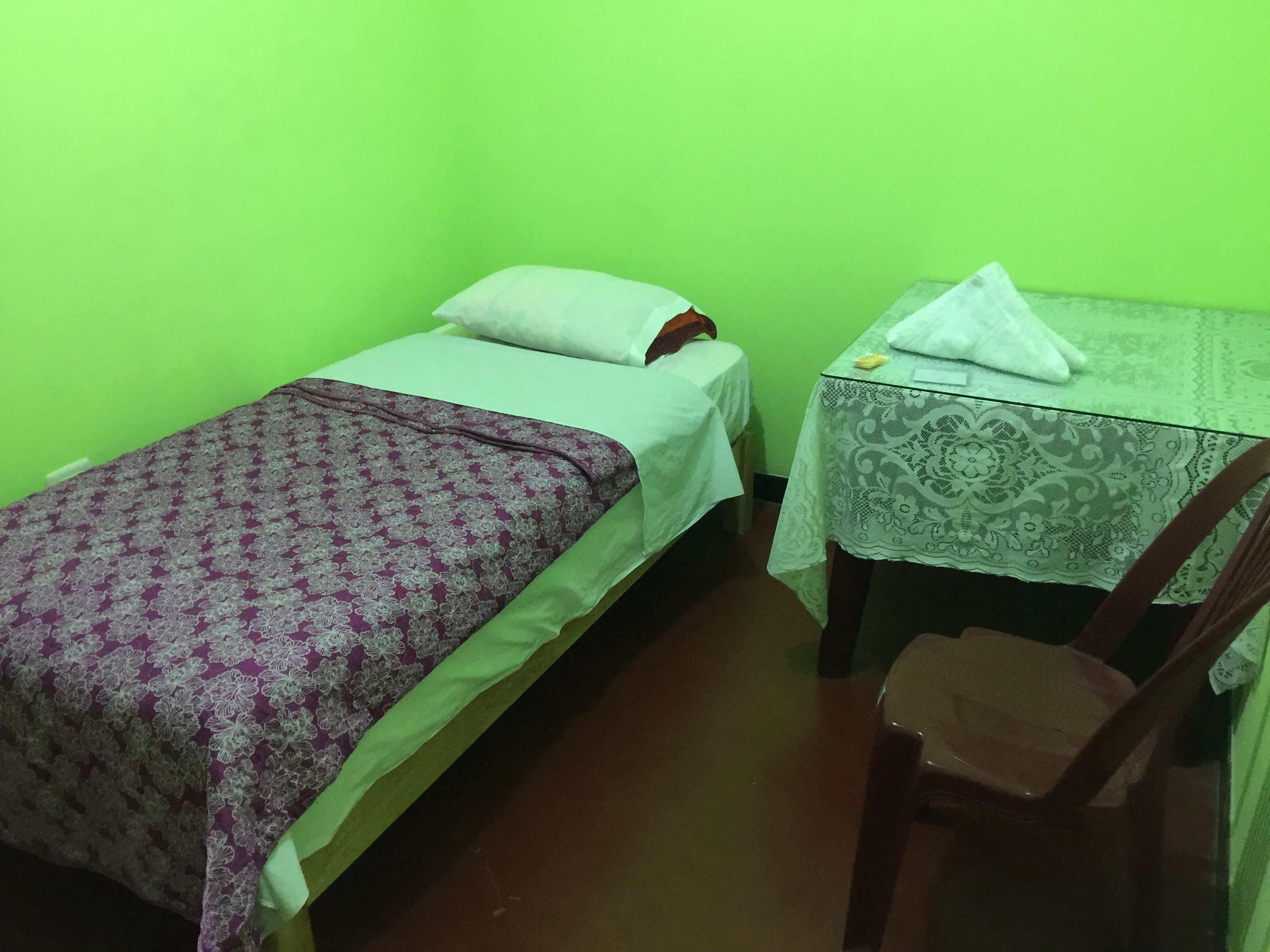 A small room with two single beds, a table with a lace tablecloth, and a chair.