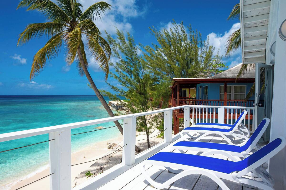 A beach view with a wooden deck, lounge chairs, and a building with a blue exterior.
