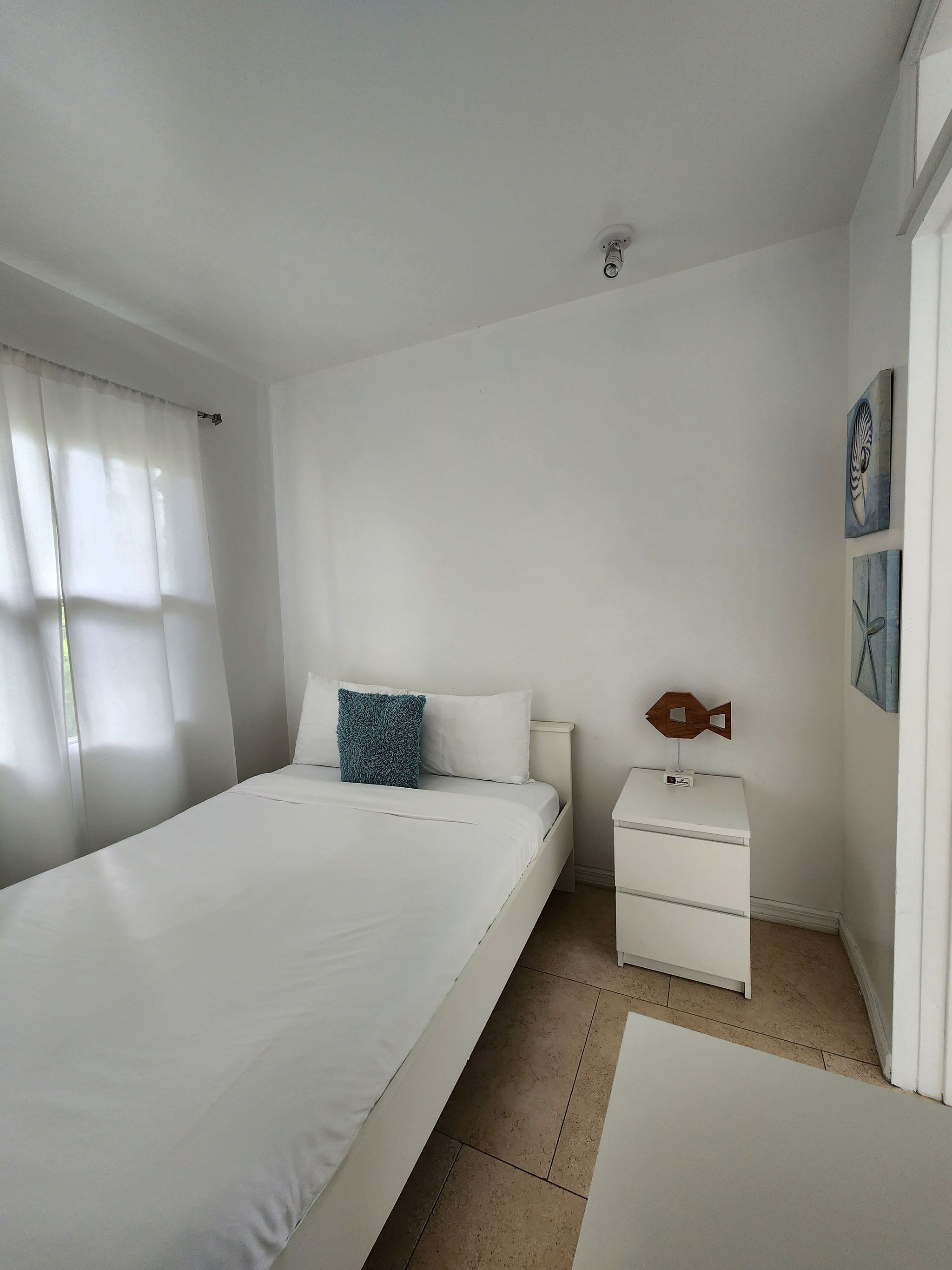 A bedroom with a bed, a nightstand, a wall clock, and a fish-shaped decoration.