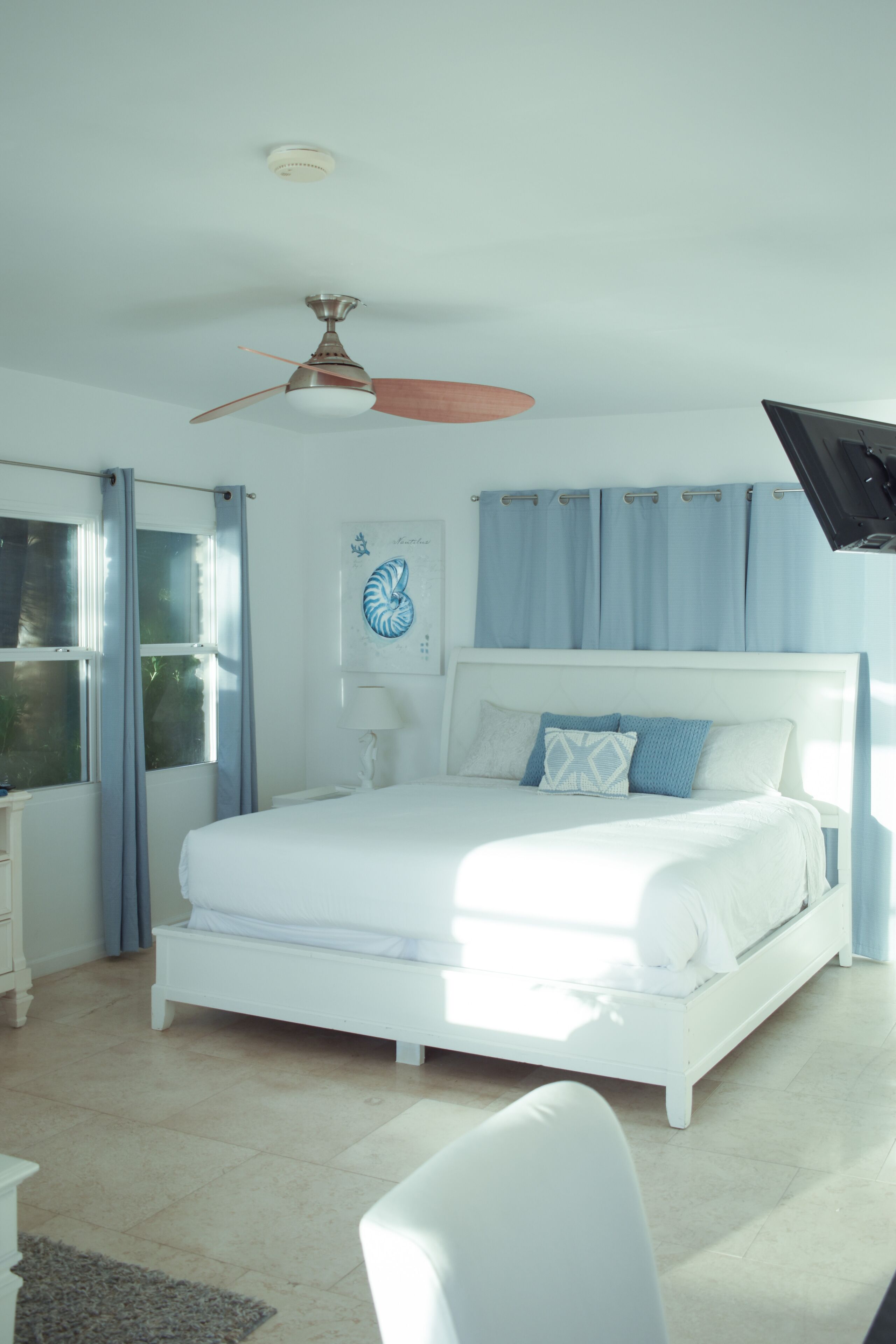 Un dormitorio con cama, ventilador de techo, ventana con cortinas y lámpara de pared.