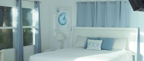 Un dormitorio con cama, ventilador de techo, ventana con cortinas y lámpara de pared.