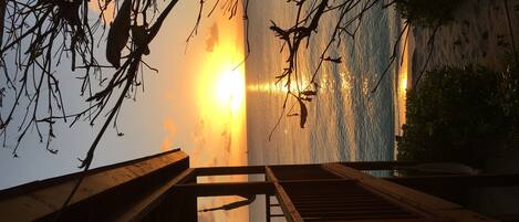 Un escalier en bois mène à un balcon d’où l’on peut admirer un coucher de soleil sur l’eau.