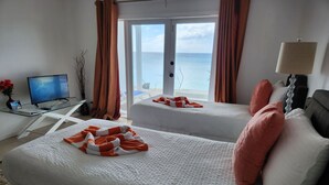 Ein Hotelzimmer mit zwei Betten, einem Schreibtisch mit Computer, einer Lampe und Meerblick.