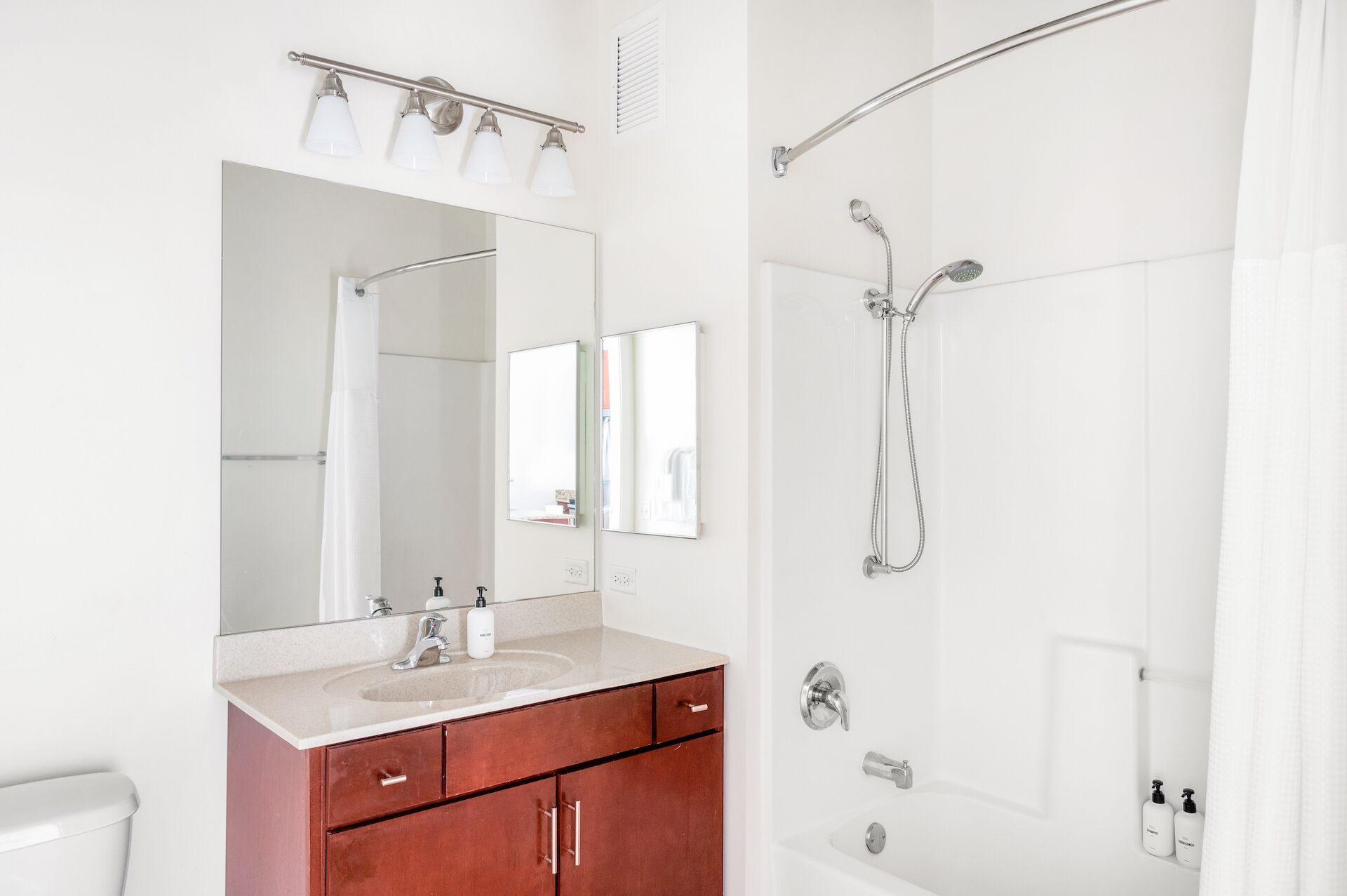 A bathroom with a large mirror, a sink, a vanity with drawers, a shower with a handheld showerhead, and a towel rack.