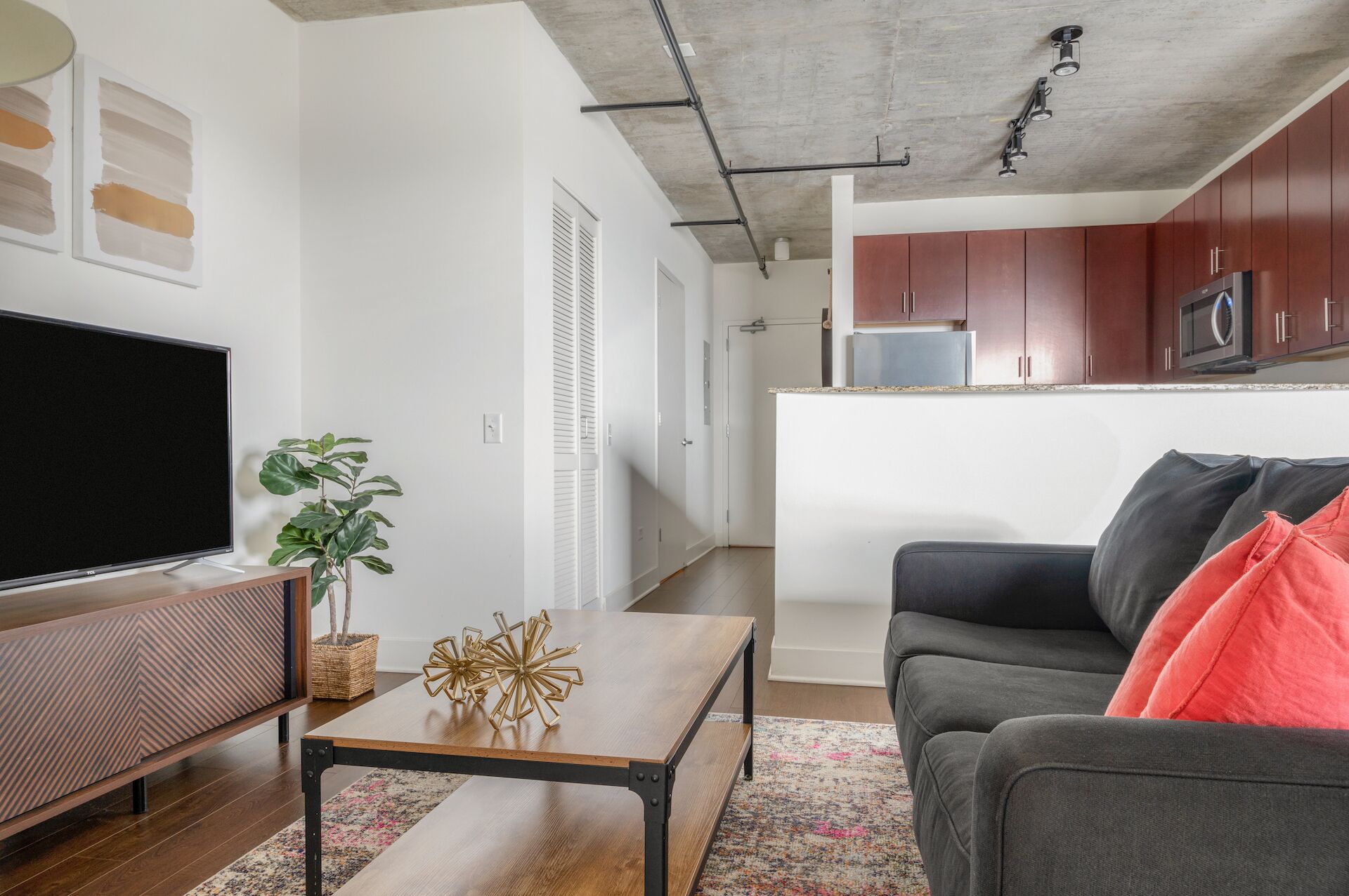 A modern living room with a flat-screen TV, a wooden coffee table, a sofa, and a kitchen in the background.