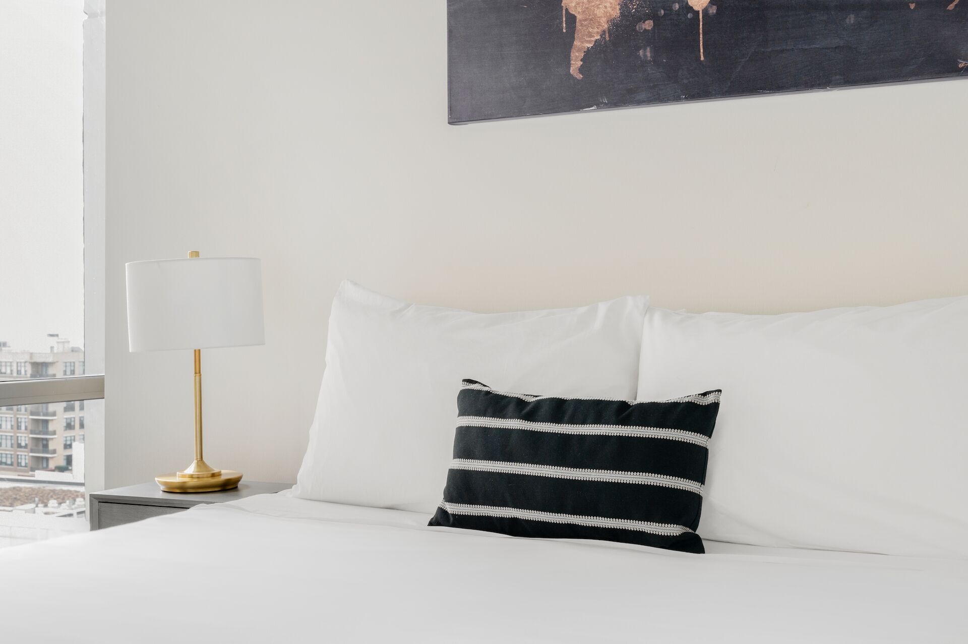 Une chambre d’hôtel avec un lit, une lampe blanche et un oreiller à rayures noires et blanches.