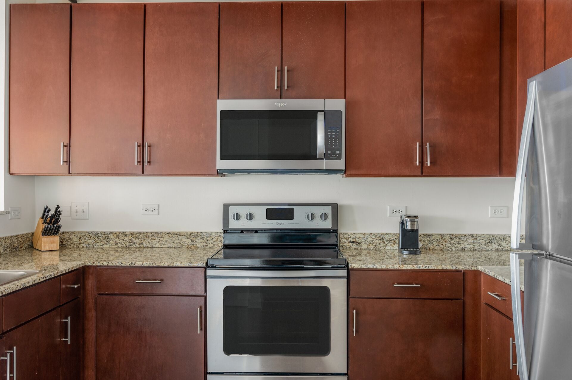 Una cocina con gabinetes marrones, un microondas de acero inoxidable, una estufa y un refrigerador.