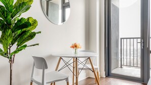 Een kamer met een witte tafel en stoel, een grote groene plant, een spiegel en uitzicht op een balkon met een leuning.