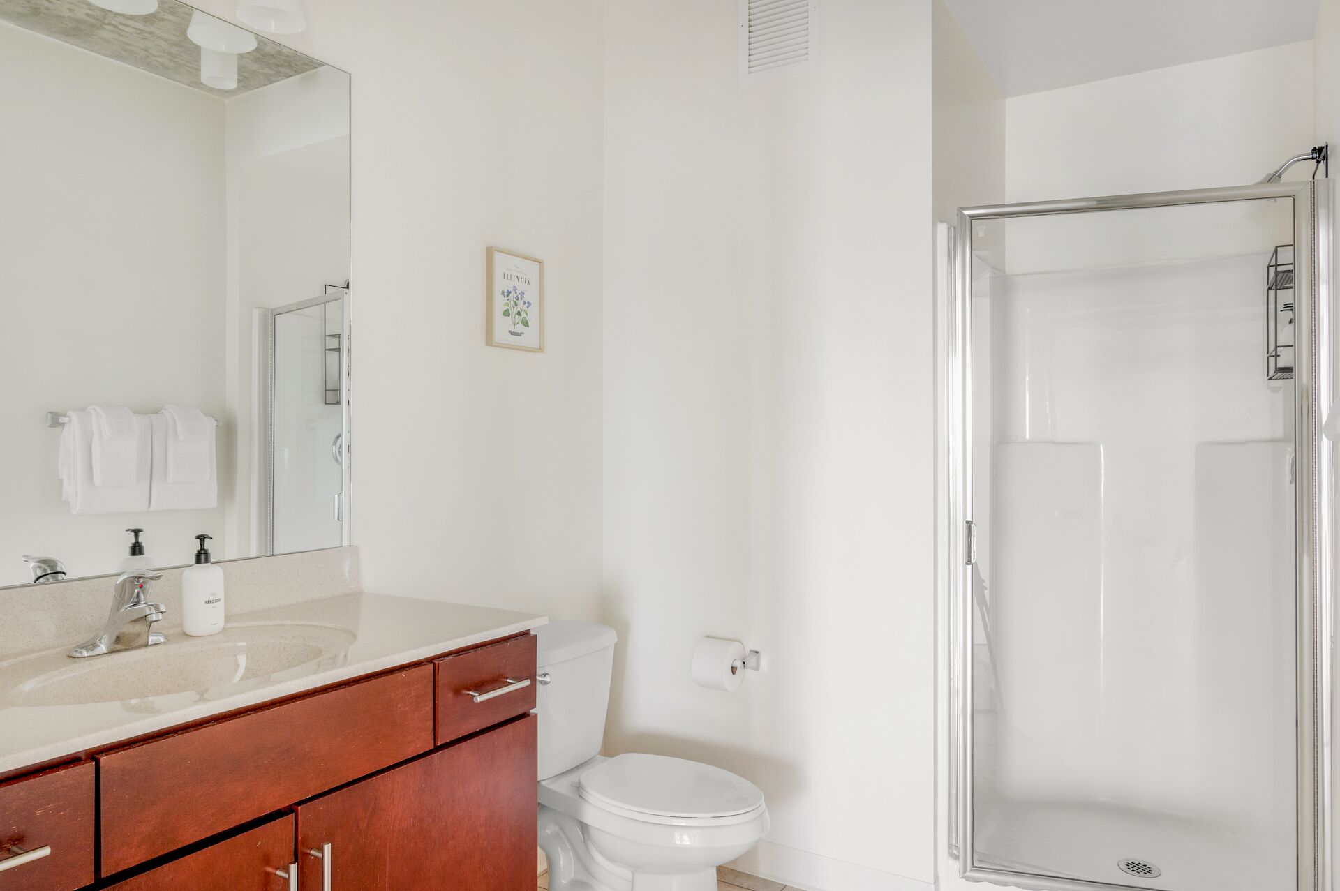 Une salle de bain avec un lavabo blanc, un miroir et des toilettes, ainsi qu’une douche à parois de verre.