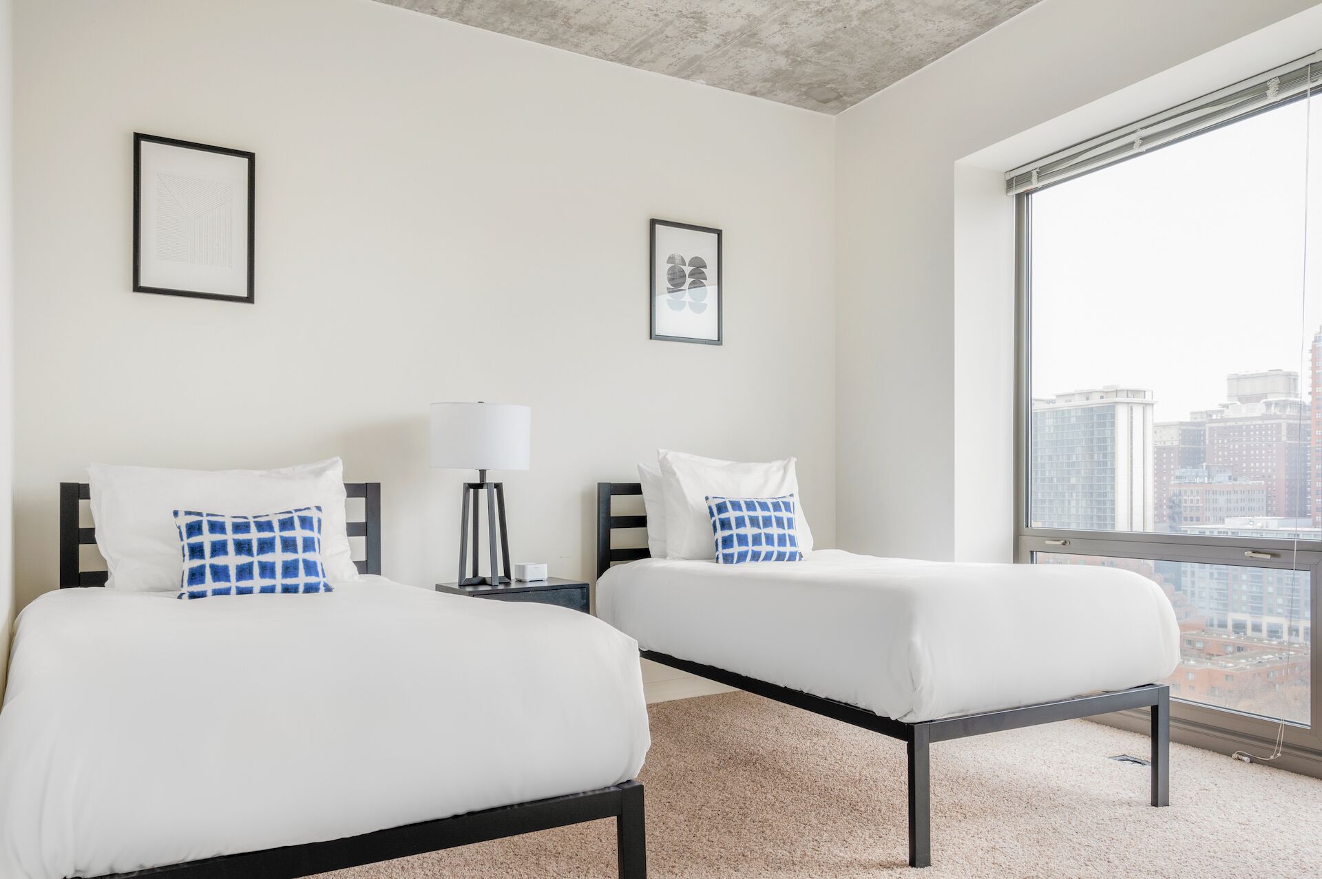Habitación de hotel con dos camas, un ventanal grande y vistas a la ciudad.