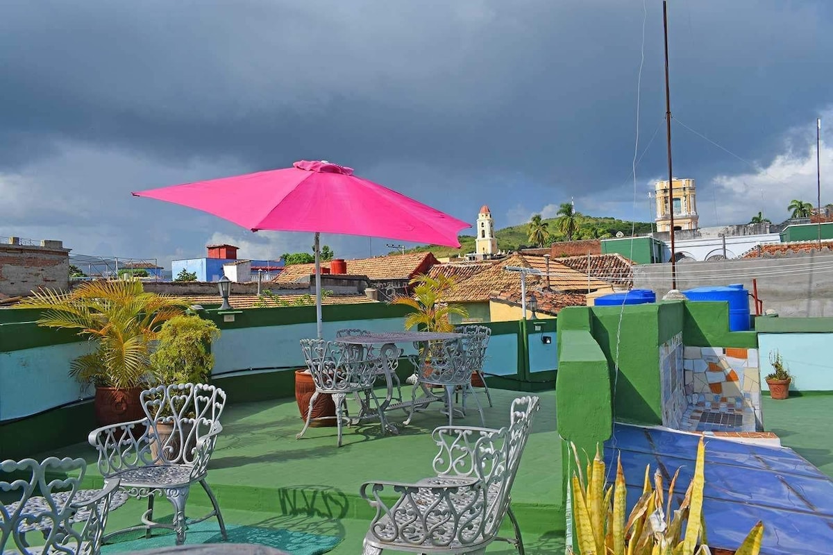 A rooftop terrace with outdoor seating, a pink umbrella, and a view of the cityscape.