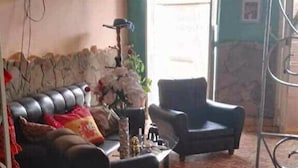Ein Wohnzimmer mit einer Couch, zwei Sesseln, einem an der Wand befestigten Fernseher und einem gemusterten Teppich.