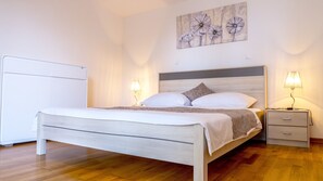 A neatly made bed with a wooden headboard, two bedside lamps, a nightstand, and a wall-mounted artwork.