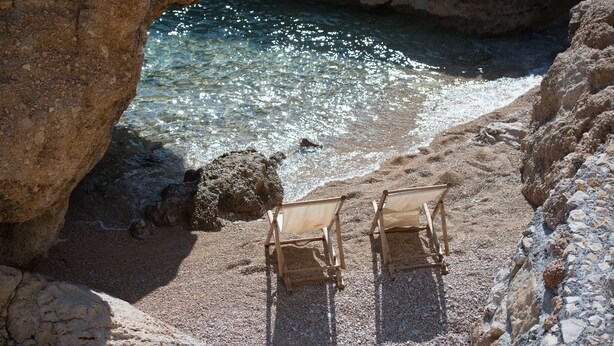 A beach with two wooden chairs and a rocky shoreline. - Apartments Andrea (Omis)