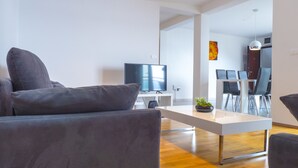 A modern living room with a flat-screen TV, grey sofas, and a wooden dining table. - Apartments Andrea (Omis)