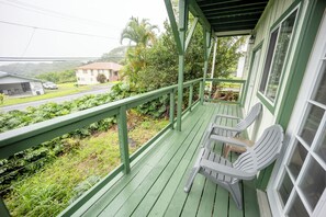 A porch with green railings, white plastic chairs, and a view of a road and buildings in the background.